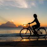 Silhouette einer Person auf einem Fahrrad am Strand bei Sonnenuntergang.
