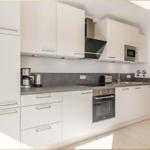 Moderne Küche mit weißen Schränken, Edelstahlgeräten und grauer Arbeitsplatte.