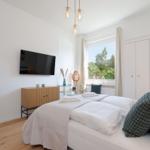 Schlafzimmer mit Bett, TV, Schreibtisch und Fenster mit Blick auf Grün.