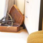 Holzkiste mit Astrolabium steht im Raum neben Schrank und Fenster.