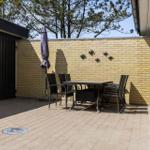 Terrasse mit Tisch, Stühlen und Sonnenschirm vor gelbem Backsteinzaun.