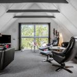 Wohnraum mit schwarzen Ledermöbeln, großem Fenster und schrägen Dachschrägen.
