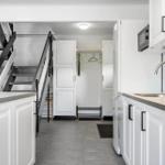 Küche mit weißen Schränken, Arbeitsfläche und Küchenzeile. Treppenhaus und Kleiderschrank im Hintergrund.