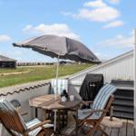 Terrasse mit Tisch, Stühlen und Sonnenschirm. Blick auf grünes Feld und Gebäude.
