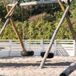 Zwei Reifen-Schaukeln an einem Holzgestell im Sand