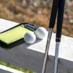 Golfclubs, zwei Bälle und ein Scorecardhalter auf einer weißen Brüstung.