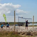 Gruppe spielt Strandvolleyball an einem sonnigen Tag am Ufer.