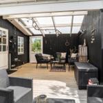 Terrasse mit Sitzgruppe, Grill und Holzboden unter Glasdach.
