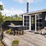 Terrasse mit Tisch, Stühlen und Schirm vor einem Haus mit Glasfront.