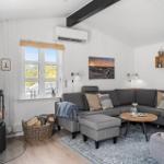 Wohnzimmer mit Kamin, Sofa und Fenster. Holzdielen und weiße Wände.