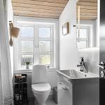 Badezimmer mit Toilette, Waschbecken und Fenster. Holzdecke und weiße Wände.