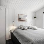 Schlafzimmer mit weiß verkleideten Wänden, Bett mit grauer Decke und Fenster.