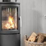 Holzofen mit brennendem Feuer und Korb mit Brennholz an der Wand.