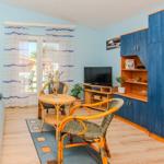 Living room with sofa, table, chairs, and TV. Blue cabinets and windows with curtains.