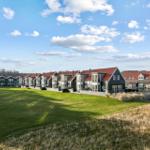 Reihen von Ferienhäusern mit roten Dächern und grünem Rasen vor blauem Himmel.