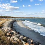 Strand mit Steinen und Wellen unter blauem Himmel mit Wolken.
