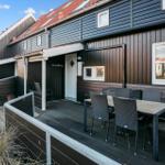 Terrasse mit Tisch und Stühlen vor einem Holzhaus mit weißen Fenstern.