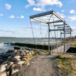 Metallbrücke mit Ketten über Steinhafen. Meer und Himmel im Hintergrund.