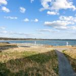 Weg führt über Brücke zum Strand mit Blick auf See und Wald.
