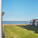 Blick auf einen grünen Rasenbereich mit See und modernen Häusern im Hintergrund.