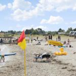 Strand mit Menschen, Rettungsschwimmer und Sonnenschirmen.