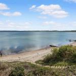 Strandufer mit Steg und sanfter Bucht unter blauem Himmel.