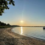 Sonnenuntergang am Strand mit Boot im Wasser und Bäumen am Ufer.