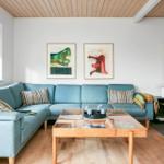 Ein Wohnzimmer mit blauem Sofa, Glas-Tisch und Wandbildern.