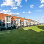 Reihenhaus mit rotem Dach und grünem Rasen vor Wasser.