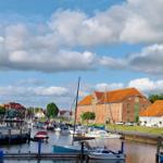 Hafen mit Booten und roten Dächern unter blauem Himmel mit Wolken.