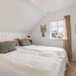 Schlafzimmer mit Dachschräge, weißem Bett und Fenster mit Vorhang.