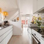 Küche mit weißen Schränken, dunklen Arbeitsflächen und gelben Lampen. Blick in Wohnbereich mit Holzboden.