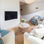 Wohnzimmer mit Sofa, Sessel und runden Tisch. Fernseher an Wand. Teppich und Beleuchtung.