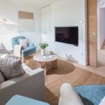 Wohnzimmer mit Sofa, Sessel, Couchtisch und Fernseher. Holzdielen und Teppichboden.