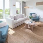 Wohnzimmer mit Sofa, Sessel und runden Tisch. Große Fenster mit Blick auf Grünfläche.