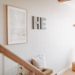 Wohnbereich mit Sessel, Wandbild und Buchstaben. Treppenhaus im Vordergrund.