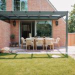 Terrasse mit Sitzgruppe unter Dach, umgeben von Gras und Steinen.