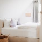 Schlafzimmer mit weißem Bett, grauen Vorhängen und einem Korb.