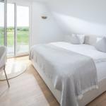 Schlafzimmer mit Bett, Stuhl und Glasfront zur Aussicht.