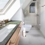 Badezimmer mit Dusche, Toilette und Waschbecken unter Dachschräge.