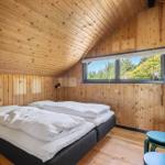 Schlafzimmer mit Doppelbett, Holzwand und Fensterblick auf Grün.