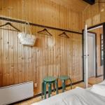 Zimmer mit Holzwand, Bett, zwei grünen Hockern und Kleiderhaken.