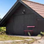 Ein dunkles Holzhaus mit rotem Dach und einer roten Stuhlbank davor.