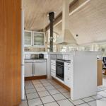 Küche mit weißer Arbeitsplatte und Holzdecke. Blick in Wohnzimmer mit Sessel.