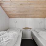Zwei Betten mit weißen Laken, Holzdecke und Fenster. Zwischen den Betten steht ein kleiner Tisch.