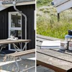 Holztisch mit Tassen und Kanne auf Terrasse vor Haus mit schwarzer Fassade.