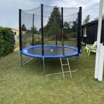 Ein Trampolin mit Sicherheitsnetz steht im Garten. Neben ihm befinden sich grüne Stühle.