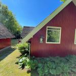 Rotes Holzhaus mit zwei Fenstern und grüner Umgebung.