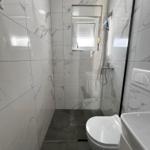 Dusche mit Duschbrause, Toilette und Waschbecken in einem Badezimmer mit Marmorfliesen.