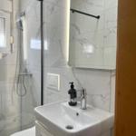 Badezimmer mit Dusche, Waschbecken und beleuchtetem Spiegel